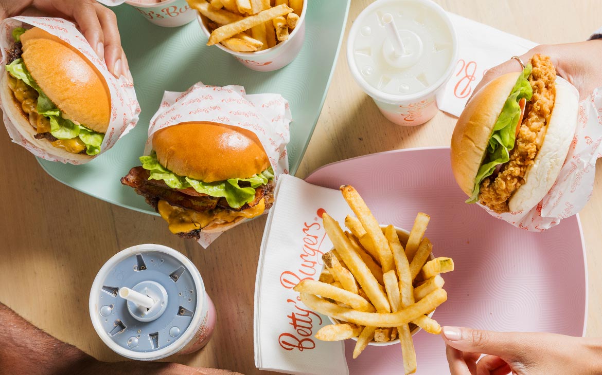 Betty's Burgers cheeseburgers, a crispy chicken burger, fries and shakes shared across a table